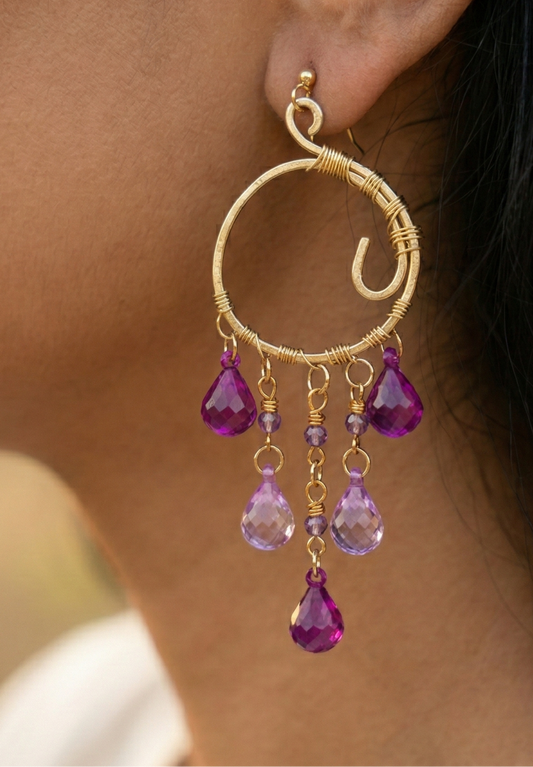 Gold hoop earring with purple gemstones worn by a person.